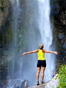 Woman hiker at waterfall with arms spread wide open