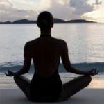 woman sitting cross-legged in yoga pose by ocean.